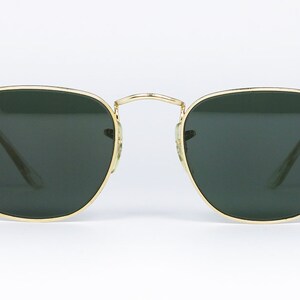 May include: Square sunglasses with gold frames and green lenses. The sunglasses feature the Ray-Ban logo on the left lens.