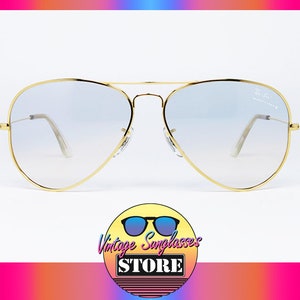 Op de afbeelding: Gouden aviator zonnebril met heldere, verlopende glazen. De zonnebril heeft een dun gouden montuur en staat op een witte achtergrond.