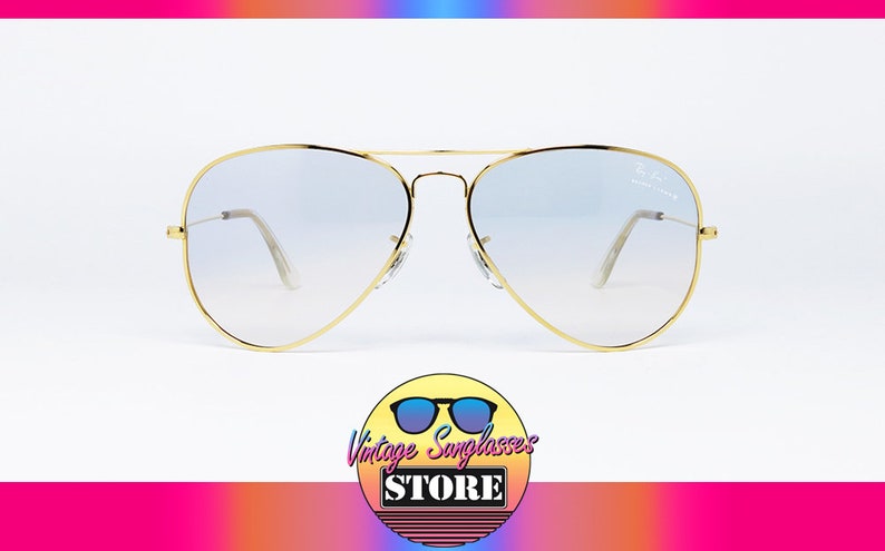 Op de afbeelding: Gouden aviator zonnebril met heldere, verlopende glazen. De zonnebril heeft een dun gouden montuur en staat op een witte achtergrond.