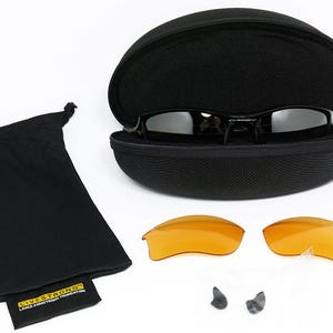 K&ouml;nnte beinhalten: Schwarze Sonnenbrille mit schwarzem Etui, zwei orangefarbenen Gl&auml;sern, einem schwarzen Kordelzugbeutel und zwei Nasenpads. Die Sonnenbrille befindet sich in einem offenen schwarzen Etui. Der Kordelzugbeutel hat ein kleines Etikett mit der Aufschrift "LIVE STRONG".