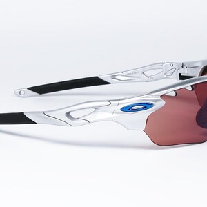 May include: Silver and black wraparound sunglasses with a blue accent on the frame and brown lenses.