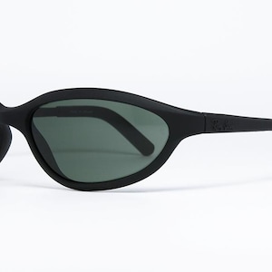 Pode incluir: &Oacute;culos de sol pretos com um design curvo e envolvente. As lentes s&atilde;o de cor verde escuro e a arma&ccedil;&atilde;o &eacute; preta fosca. O logotipo da Ray-Ban &eacute; vis&iacute;vel na haste. Estes &oacute;culos de sol s&atilde;o projetados para esportes e atividades ao ar livre.