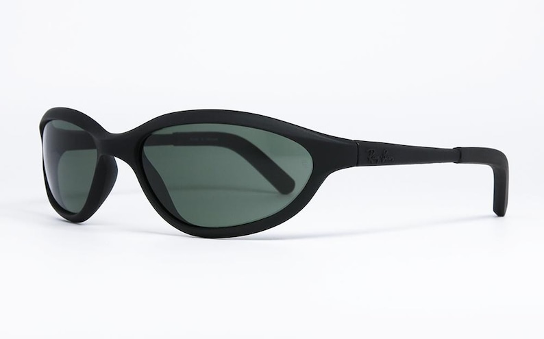 Pode incluir: &Oacute;culos de sol pretos com um design curvo e envolvente. As lentes s&atilde;o de cor verde escuro e a arma&ccedil;&atilde;o &eacute; preta fosca. O logotipo da Ray-Ban &eacute; vis&iacute;vel na haste. Estes &oacute;culos de sol s&atilde;o projetados para esportes e atividades ao ar livre.