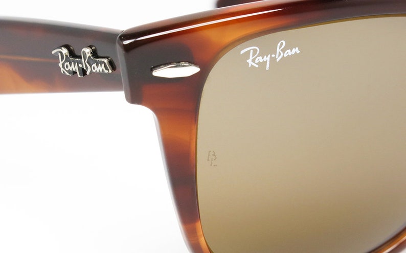 Peut inclure: Gros plan sur une paire de lunettes de soleil Ray-Ban en &eacute;caille de tortue brune avec des verres bruns. Le logo Ray-Ban est visible sur la lentille droite.