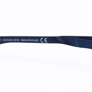 K&ouml;nnte beinhalten: Nahaufnahme des B&uuml;gels einer Brille. Der B&uuml;gel ist matt marineblau mit dem Text "141 OX3232-0454 Matte Midnight" aufgedruckt. Das Ende des B&uuml;gels ist wei&szlig;. Das CE-Zeichen ist sichtbar.