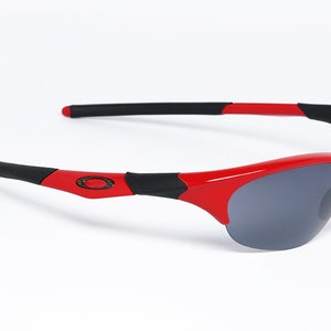 Puede incluir: Gafas de sol rojas y negras con un dise&ntilde;o deportivo. Las gafas tienen una montura roja brillante con detalles negros en las patillas. Las lentes son de color gris oscuro, ofreciendo protecci&oacute;n solar. Un accesorio de moda.