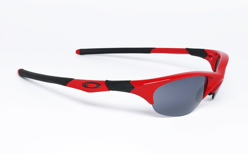 Puede incluir: Gafas de sol rojas y negras con un dise&ntilde;o deportivo. Las gafas tienen una montura roja brillante con detalles negros en las patillas. Las lentes son de color gris oscuro, ofreciendo protecci&oacute;n solar. Un accesorio de moda.