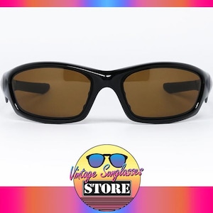 May include: Black sunglasses with brown lenses. The sunglasses have a curved frame and a sporty design. The image includes a logo for a vintage sunglasses store.