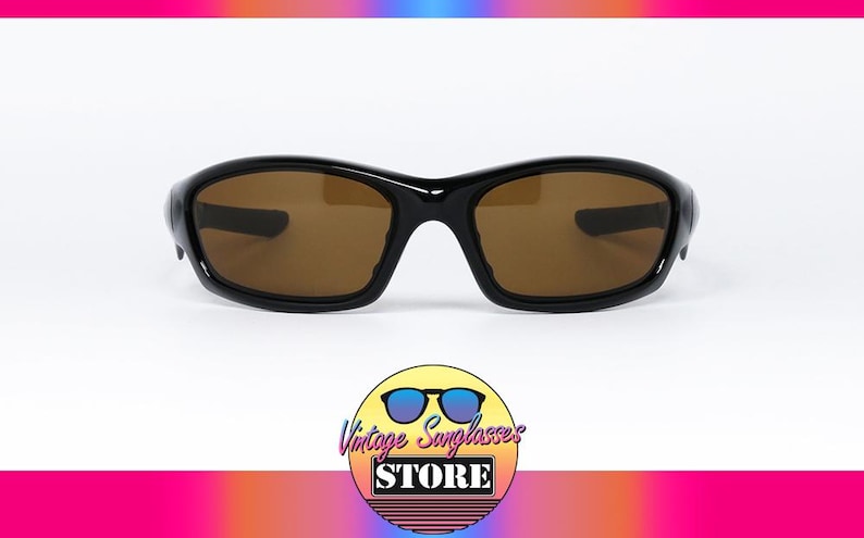 May include: Black sunglasses with brown lenses. The sunglasses have a curved frame and a sporty design. The image includes a logo for a vintage sunglasses store.