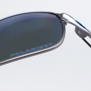 May include: Close-up of polarized sunglasses with a silver frame and blue lenses. The word "POLARIZED" is printed in blue on the lens. The sunglasses have a modern, sporty design.