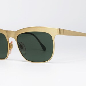 Puede incluir: Gafas de sol doradas con lentes verde oscuro. Las monturas tienen un dise&ntilde;o distintivo de cejas y patillas elegantes. Las lentes son de color verde oscuro y las gafas de sol tienen un estilo cl&aacute;sico y atemporal.