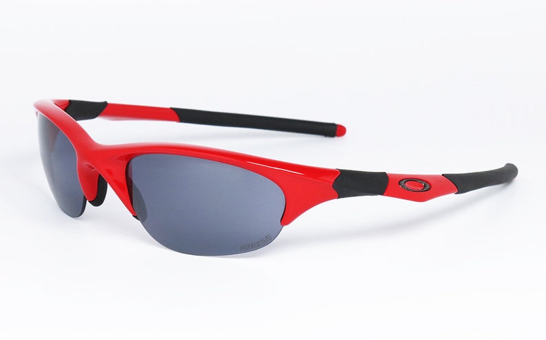 Puede incluir: Gafas de sol rojas y negras con lentes grises. Las gafas tienen un dise&ntilde;o deportivo con montura roja y detalles negros en las patillas. El logotipo de Oakley es visible en la patilla.