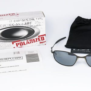 Może przedstawiać: Słoneczne okulary polaryzacyjne z czarną oprawką i szarymi soczewkami, obok czarnego woreczka ze sznurkiem i białego pudełka z napisem "POLARIZED" w kolorze czerwonym. Obecny jest r&oacute;wnież formularz odpowiedzi biznesowej.