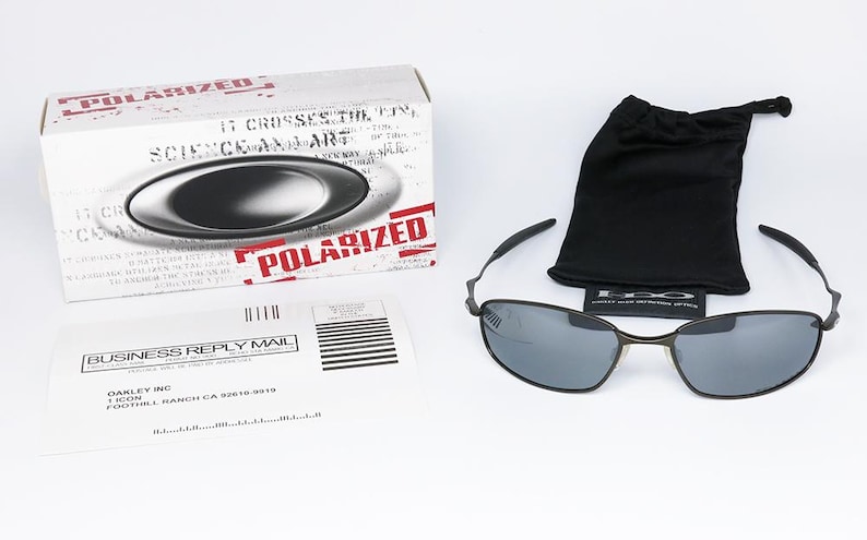 Może przedstawiać: Słoneczne okulary polaryzacyjne z czarną oprawką i szarymi soczewkami, obok czarnego woreczka ze sznurkiem i białego pudełka z napisem "POLARIZED" w kolorze czerwonym. Obecny jest r&oacute;wnież formularz odpowiedzi biznesowej.