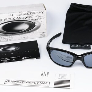 May include: Black sunglasses with gray lenses, a black carrying pouch, and a box with the brand logo. The sunglasses are displayed on a white surface. Also included is a warranty card and a business reply mail envelope.