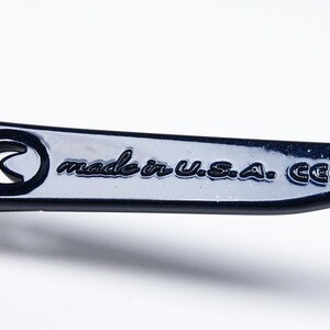 May include: Close-up of a dark blue metal object with the text "made in U.S.A. CE". The object has a curved design with a circular cutout. The surface is glossy and reflects light.