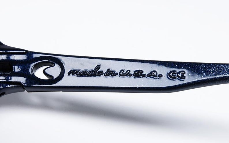 May include: Close-up of a dark blue metal object with the text "made in U.S.A. CE". The object has a curved design with a circular cutout. The surface is glossy and reflects light.