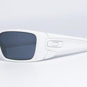 May include: White sunglasses with dark grey lenses. The sunglasses have a rectangular shape and a modern design. The frame is a solid white colour, and the lenses are a dark grey. The sunglasses are set against a white background.
