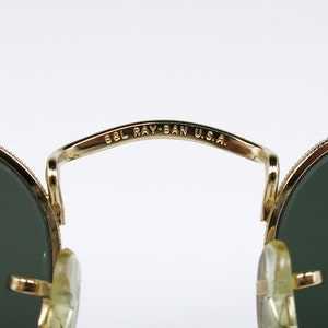 May include: Close-up of the gold-tone metal bridge of a pair of Ray-Ban sunglasses. The bridge is inscribed with "B&L RAY-BAN U.S.A."