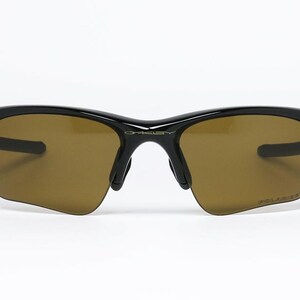 May include: Black sunglasses with brown tinted lenses. The sunglasses have a sleek, modern design with a curved frame and the word "POLARIZED" printed on the lens. The brand name "OAKLEY" is visible on the bridge.
