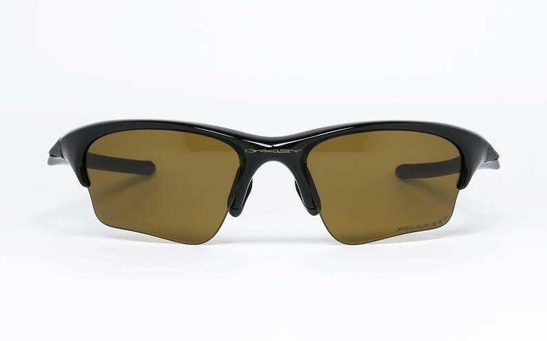 May include: Black sunglasses with brown tinted lenses. The sunglasses have a sleek, modern design with a curved frame and the word "POLARIZED" printed on the lens. The brand name "OAKLEY" is visible on the bridge.