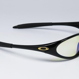 Peut inclure: Lunettes de soleil noires avec une finition brillante. Les verres ont une teinte jaune. Les montures pr&eacute;sentent un logo dor&eacute; sur les branches. Les branches sont incurv&eacute;es.