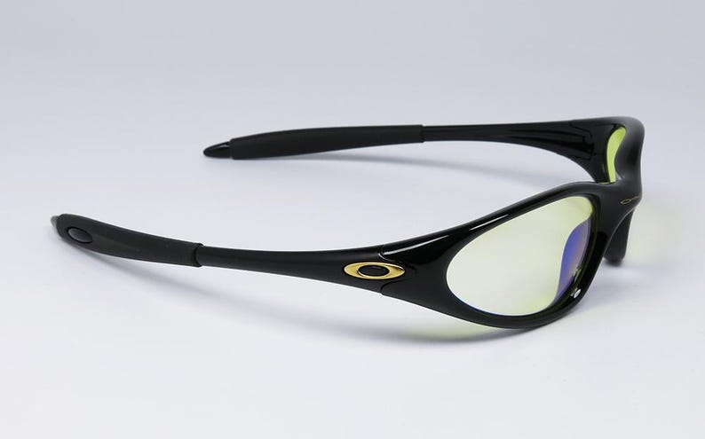 Peut inclure: Lunettes de soleil noires avec une finition brillante. Les verres ont une teinte jaune. Les montures pr&eacute;sentent un logo dor&eacute; sur les branches. Les branches sont incurv&eacute;es.