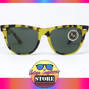May include: Sunglasses with a yellow and black tortoise shell pattern frame and dark lenses. The sunglasses have a classic design with a round sticker on the right lens. The image includes a logo for a vintage sunglasses store.