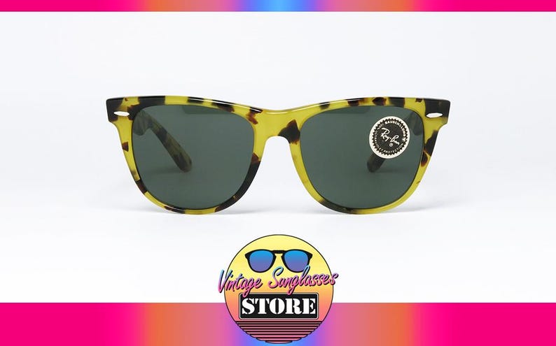 May include: Sunglasses with a yellow and black tortoise shell pattern frame and dark lenses. The sunglasses have a classic design with a round sticker on the right lens. The image includes a logo for a vintage sunglasses store.