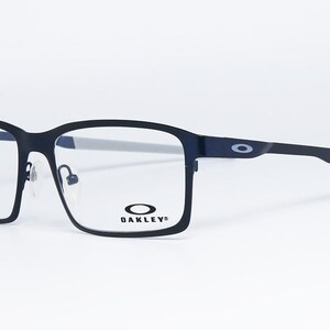 K&ouml;nnte beinhalten: Schwarze rechteckige Brille mit grauen B&uuml;geln. Die Brille hat eine matte Oberfl&auml;che und das Oakley-Logo ist auf dem Rahmen und dem B&uuml;gel sichtbar. Die Gl&auml;ser sind klar.