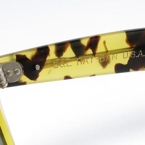 May include: Close-up of the arm of a pair of sunglasses with a tortoise shell pattern. The text "B&L RAY-BAN U.S.A." is printed on the inside of the arm. The hinge is visible.
