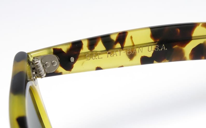 May include: Close-up of the arm of a pair of sunglasses with a tortoise shell pattern. The text "B&L RAY-BAN U.S.A." is printed on the inside of the arm. The hinge is visible.