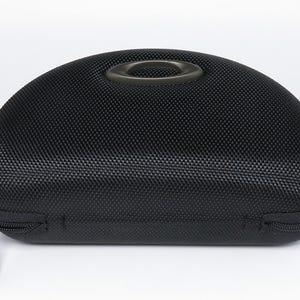 May include: Black, semi-hard sunglasses case with a textured surface and a zipper closure. The case has a handle on top and a black zipper pull. The case is designed to protect eyewear.
