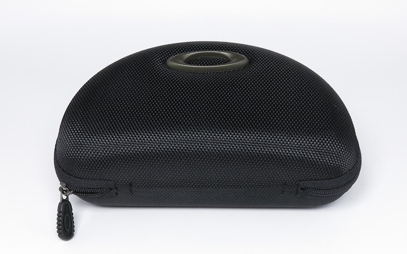 May include: Black, semi-hard sunglasses case with a textured surface and a zipper closure. The case has a handle on top and a black zipper pull. The case is designed to protect eyewear.