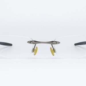 May include: A pair of rimless eyeglasses with a silver frame and clear lenses. The glasses have a simple, modern design.