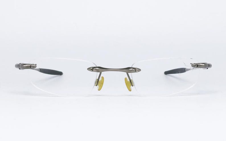 May include: A pair of rimless eyeglasses with a silver frame and clear lenses. The glasses have a simple, modern design.