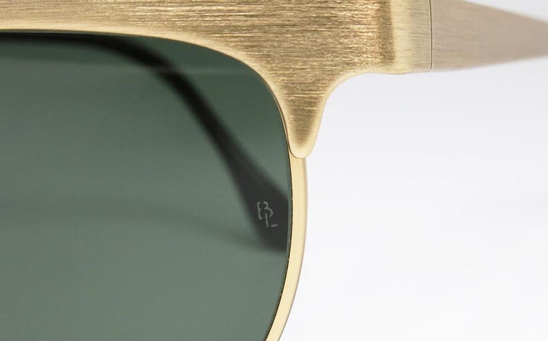 Puede incluir: Primer plano de gafas de sol doradas con lentes verdes. La montura tiene un acabado texturizado. Las gafas de sol tienen un peque&ntilde;o logotipo grabado en la lente.