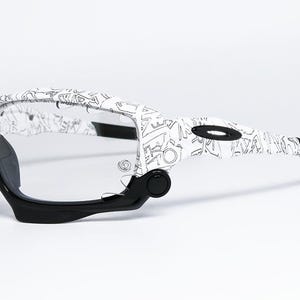 May include: White and black patterned sunglasses with clear lenses. The frames feature a unique design with black accents on the arms and nose bridge. The sunglasses are designed for sports and outdoor activities.