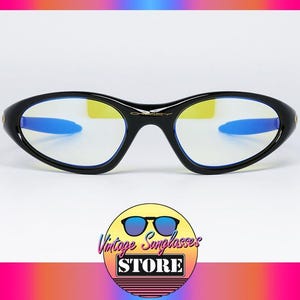 Peut inclure: Lunettes de soleil Oakley noires avec une monture incurv&eacute;e et des accents bleus sur les branches. Les verres ont une teinte jaune. Les lunettes de soleil sont affich&eacute;es sur un fond blanc. Le logo de Vintage Sunglasses Store est en bas.