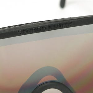Op de afbeelding: Close-up van een zwarte zonnebril met een reflecterende lens. De merknaam, BAUSCH & LOMB, is in de bovenkant van het montuur ge&euml;mbosseerd. De lenzen hebben een kleurengradi&euml;nt.