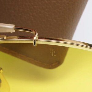 K&ouml;nnte beinhalten: Nahaufnahme einer goldenen Sonnenbrille mit gelben Gl&auml;sern. Die Sonnenbrille ist zusammengeklappt und liegt auf einem braunen Lederetui.