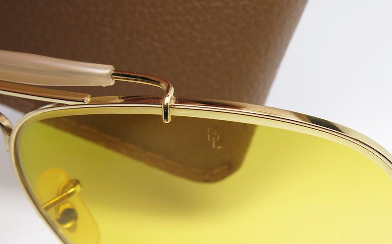 K&ouml;nnte beinhalten: Nahaufnahme einer goldenen Sonnenbrille mit gelben Gl&auml;sern. Die Sonnenbrille ist zusammengeklappt und liegt auf einem braunen Lederetui.
