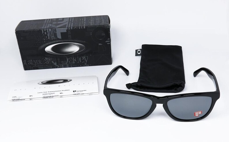 May include: Black sunglasses with gray lenses, a black case, a black drawstring pouch, and a white card. The sunglasses have a red logo on the bottom right lens. The case has the brand name and logo.