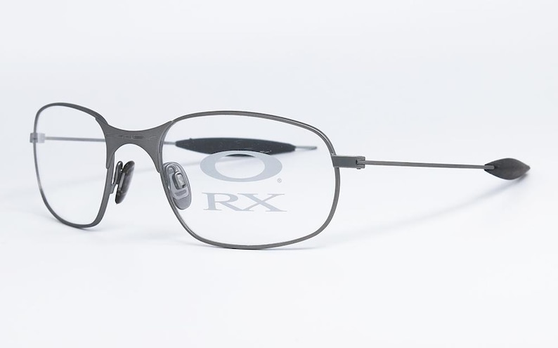 May include: Gray metal frame eyeglasses with clear lenses. The lenses have the text "O RX" printed on them.