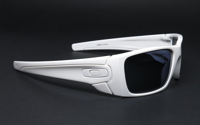 May include: White sunglasses with dark lenses. The sunglasses have a rectangular frame with a curved design. The arms of the sunglasses are thick and have a slight curve. The lenses are dark, and the frame is white.