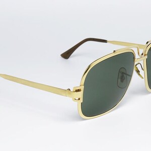 Puede incluir: Gafas de sol doradas con lentes verde oscuro. Las gafas de sol tienen un dise&ntilde;o cl&aacute;sico de aviador con doble puente y forma rectangular. Las patillas son finas y doradas, con puntas marrones. Las lentes son de color verde oscuro.