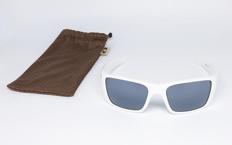 May include: White sunglasses with grey lenses and a brown drawstring pouch. The sunglasses have a rectangular frame and a modern design. The pouch is made of a soft, textured material.