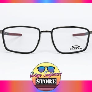 May include: Black framed Oakley eyeglasses with a rectangular shape. The temples have a red accent. The Oakley logo is visible on the right lens. The background is white with a colorful gradient.