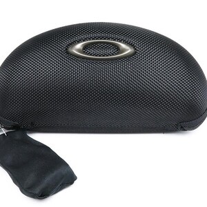 May include: Black, textured eyewear case with a silver-tone Oakley logo. The case has a zipper closure and includes a small black pouch. The case is designed to protect eyeglasses or sunglasses.