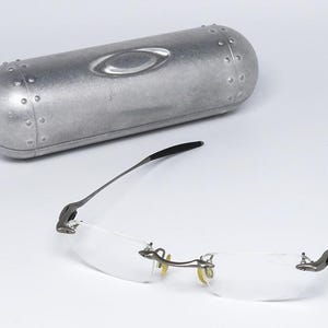 May include: A pair of silver-toned rimless glasses with clear lenses and a silver metal case.